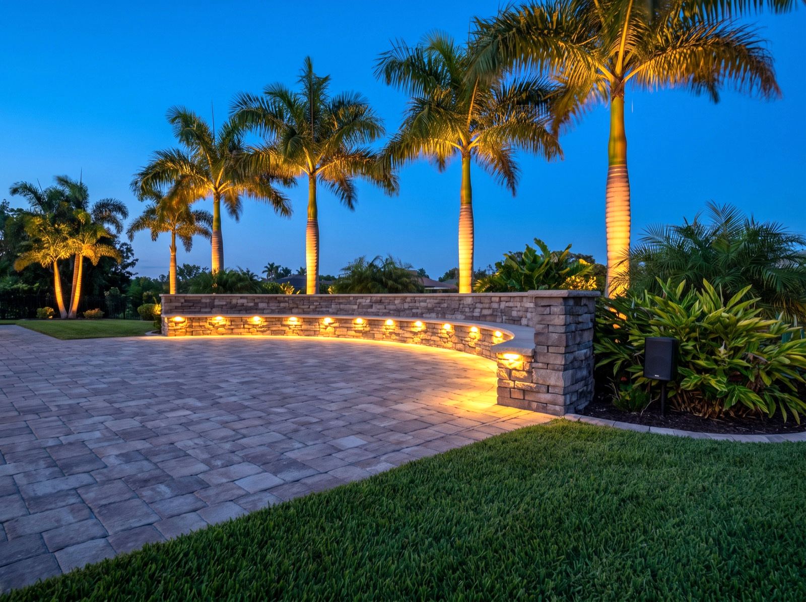 A paver patio and seat wall at dusk with integrated warm lighting and a speaker set into the planting