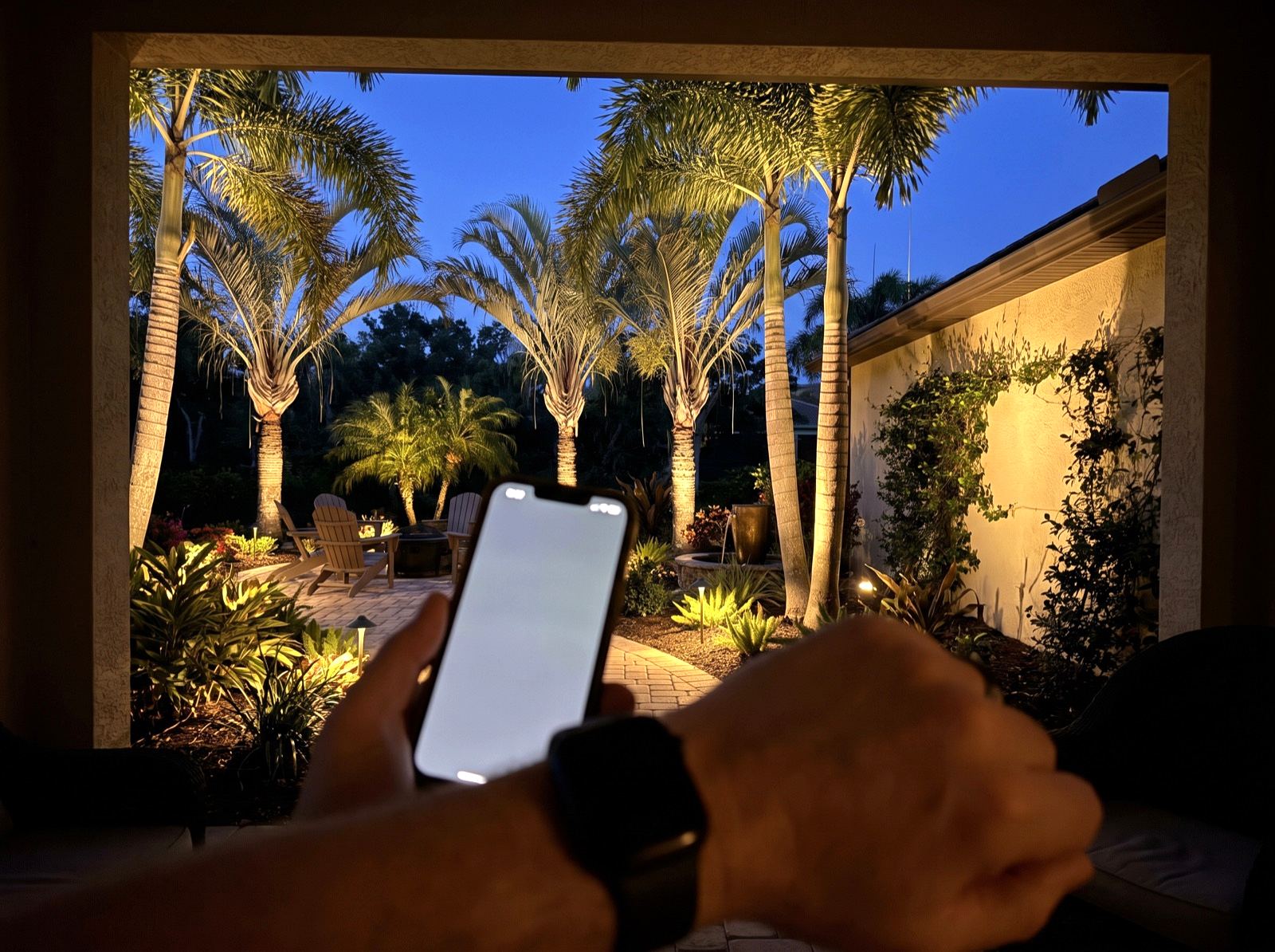 Adjusting a warmly lit garden from a phone on the lanai at blue hour